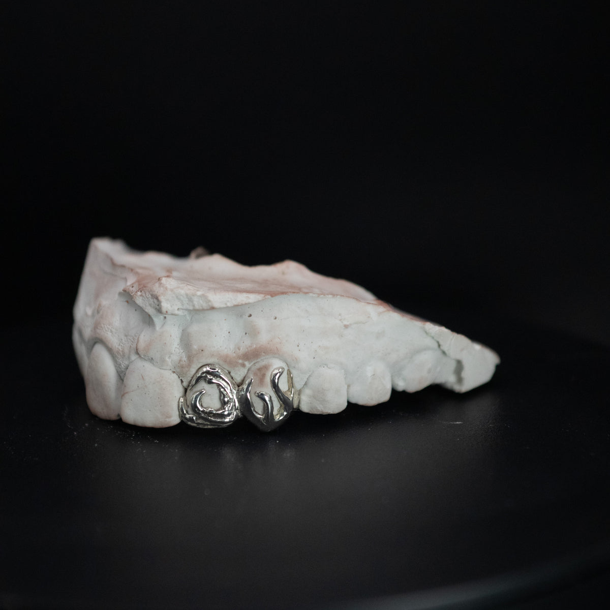 A set of silver and gold-coloured grillz with fire and water design on a dark background