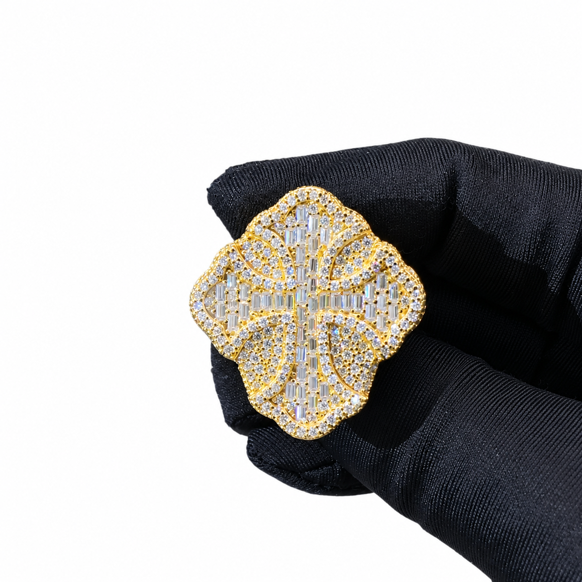 A gold-toned floral brooch or pin embellished with clear crystals, held by a hand wearing a black textured glove against a plain white background.