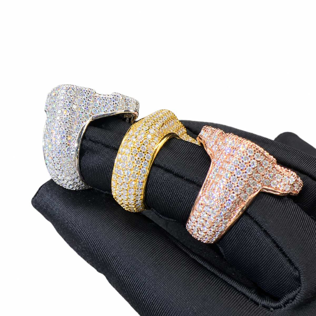 Three oversized ring-shaped cuff bracelets covered in pavé crystals, shown on a black fabric display against a white background. The bracelets are in silver, yellow gold, and rose gold tones.