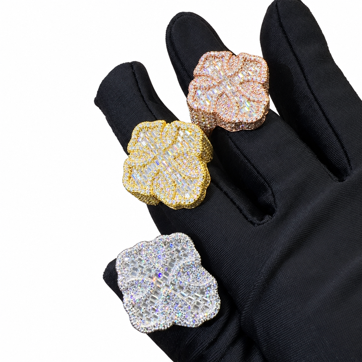 Three flower-shaped statement rings with pavé-set clear stones, shown on a black glove against a white background.