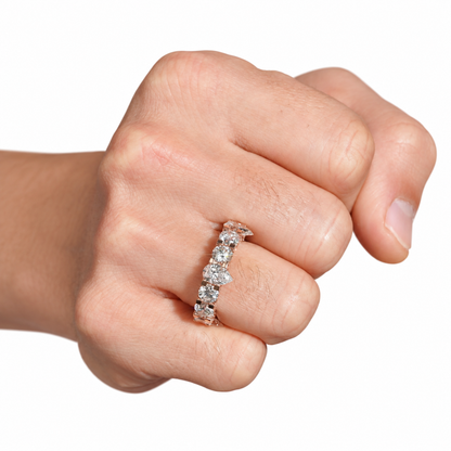 A close-up of a person's hand wearing a silver-toned eternity ring set with clear round-cut gemstones, shown against a plain white background.
