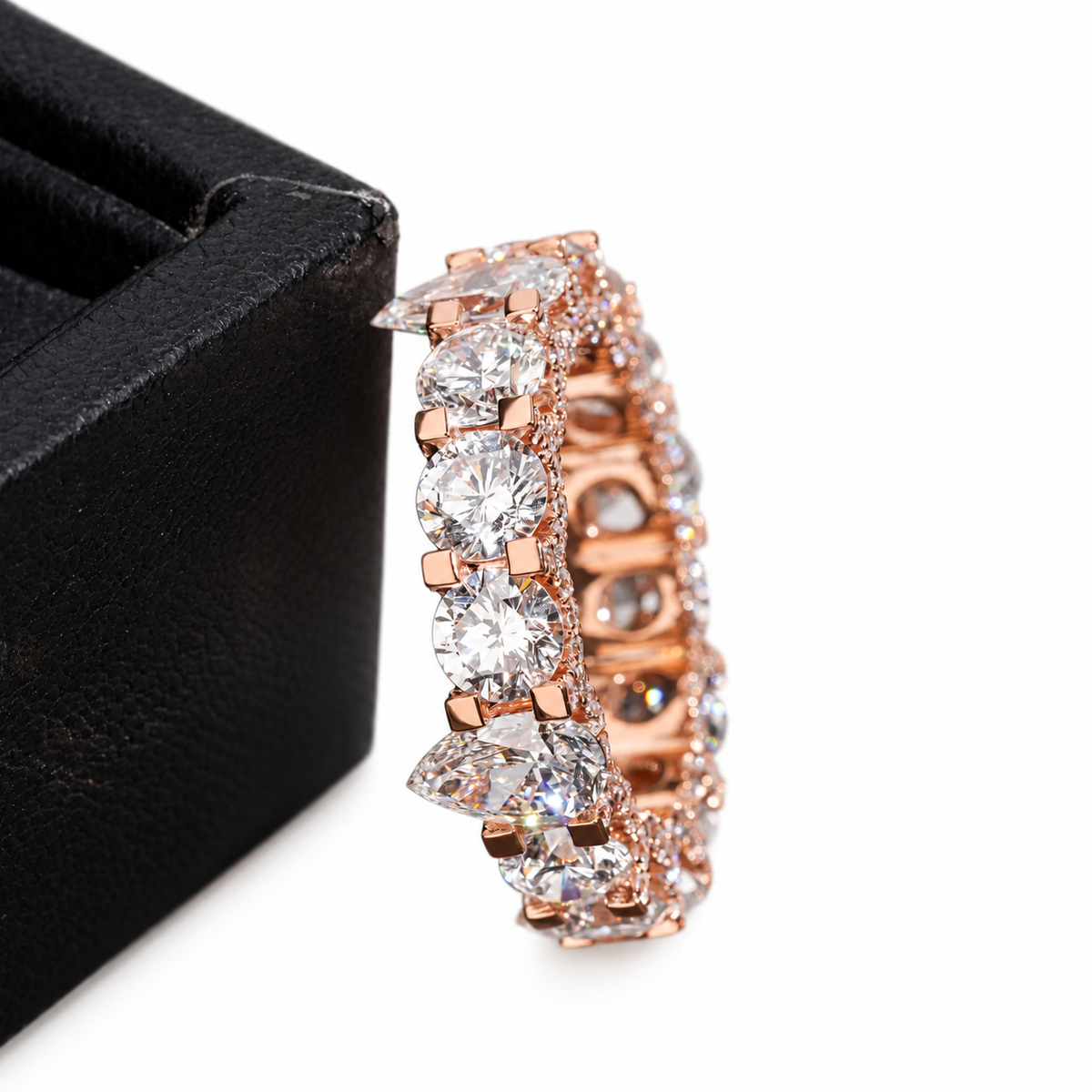A rose gold eternity ring with clear round and marquise-cut gemstones, displayed next to a black jewelry box on a white background.