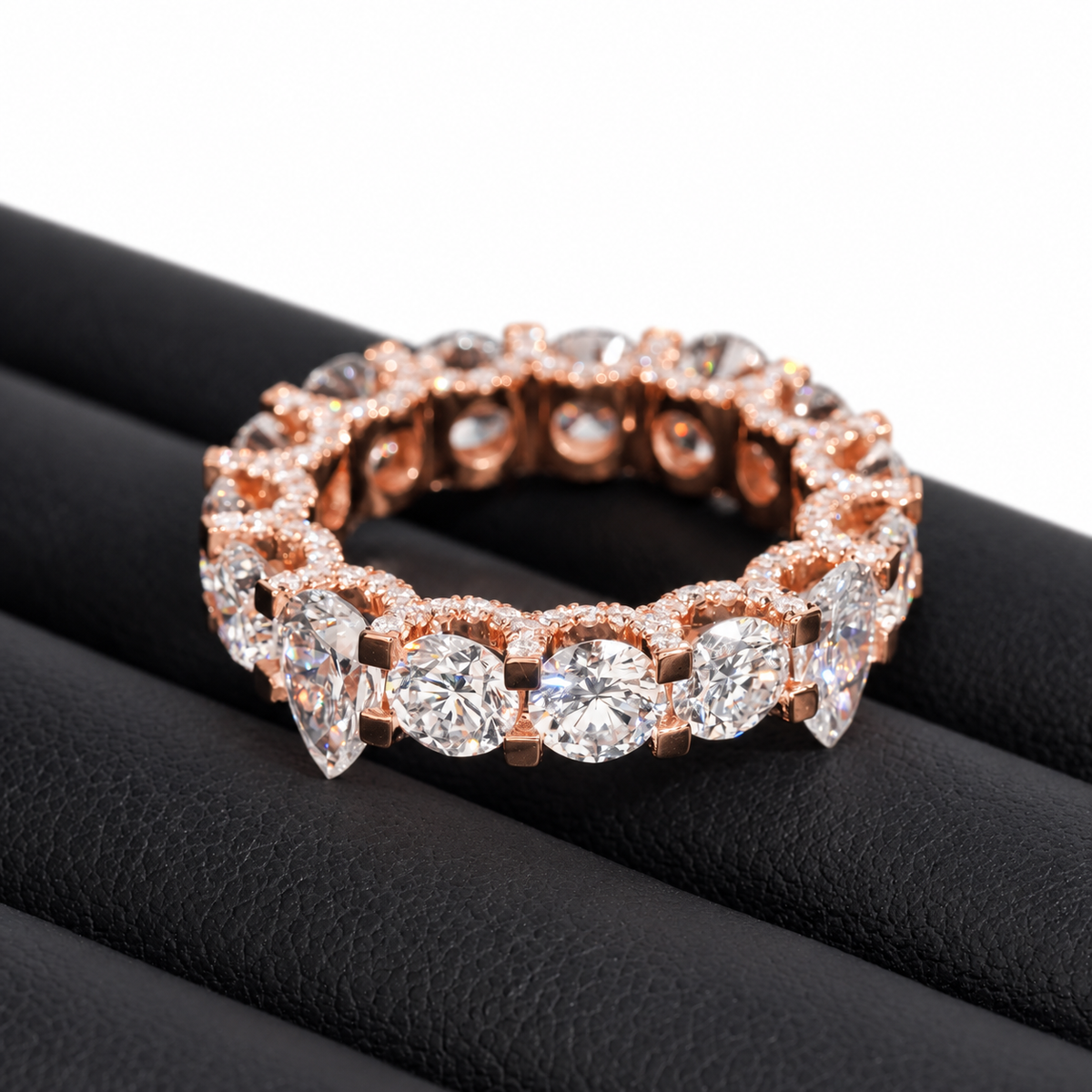 A rose gold eternity ring set with round and marquise-cut clear gemstones, displayed on a black textured ring stand against a white background.