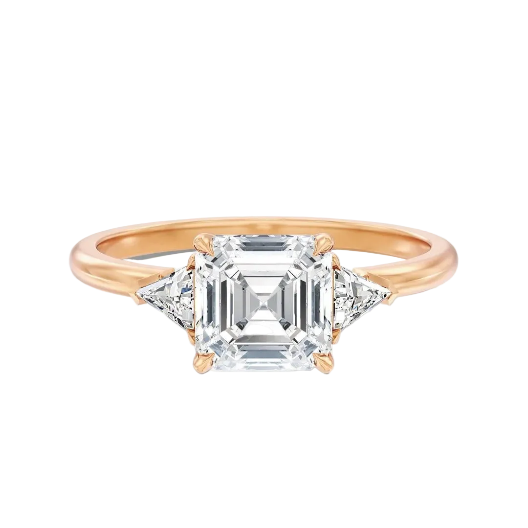 A rose gold engagement ring featuring a central emerald-cut diamond surrounded by two smaller round diamonds, set on a polished rose gold band against a clean white background.